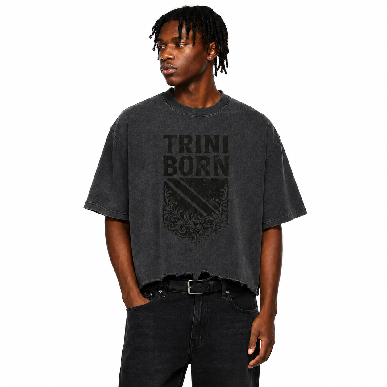 Black male model wearing the Trini Born Culture Tee in vintage black featuring a gray distressed TRINI BORN crest graphic on the front, oversized boxy fit with cropped distressed hem on a clean white studio background.
