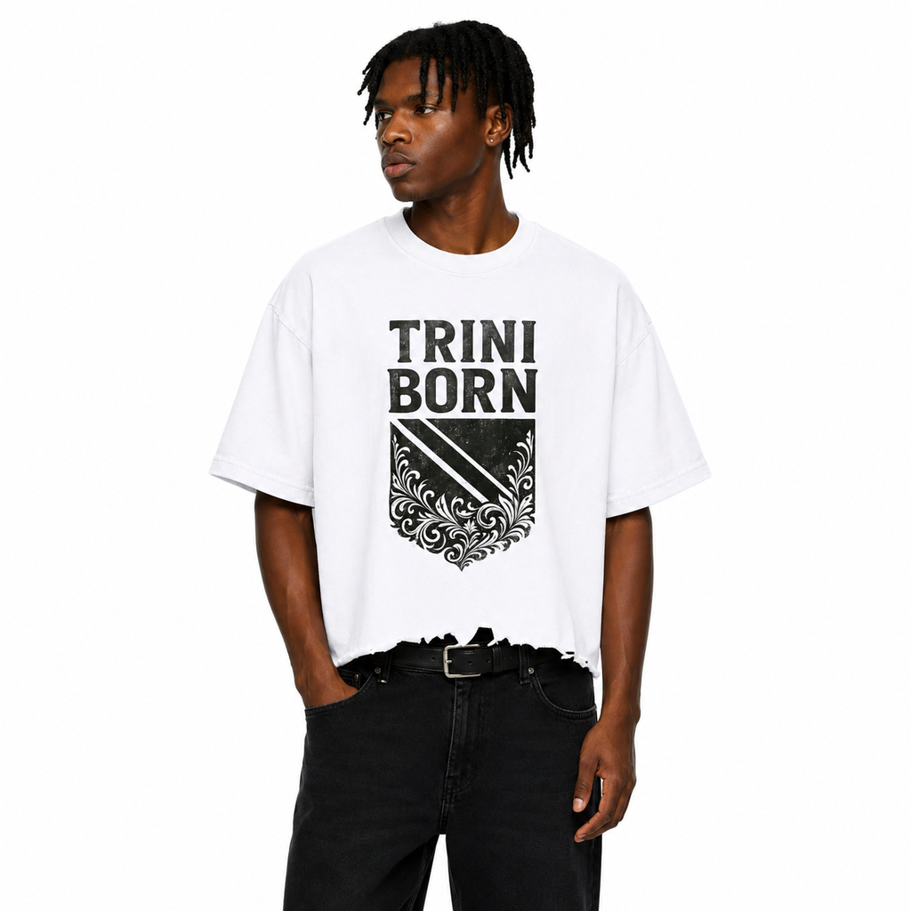 Black male model wearing the Trini Born Culture Tee in white featuring the black distressed TRINI BORN crest graphic on the front, oversized boxy cropped fit with distressed hem on a white studio background.