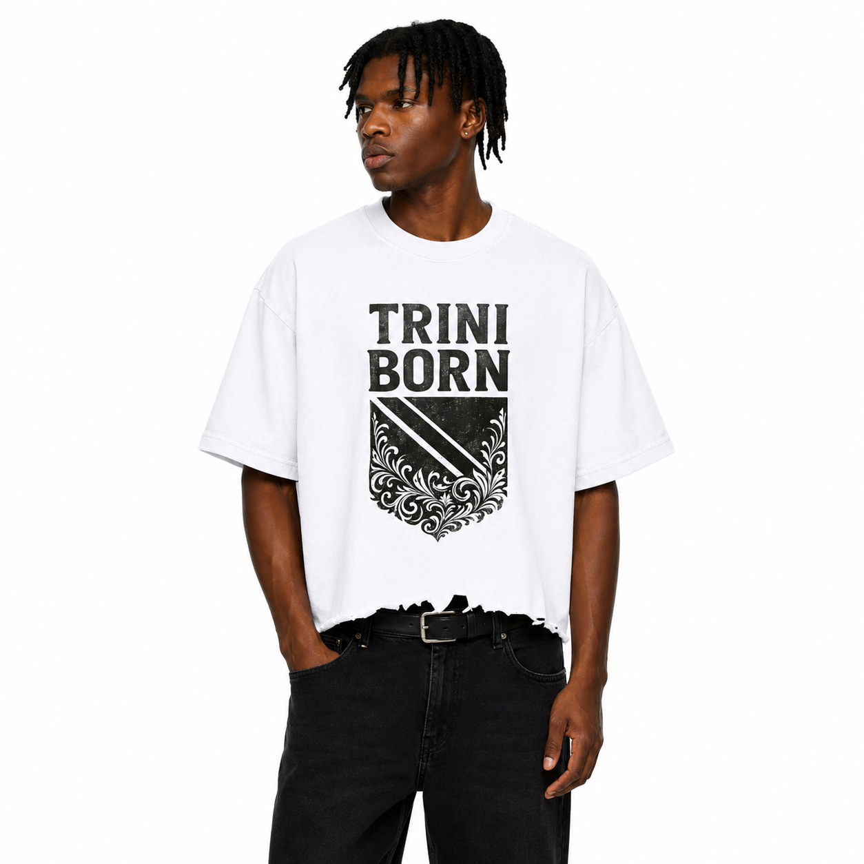 Black male model wearing the Trini Born Culture Tee in white featuring the black distressed TRINI BORN crest graphic on the front, oversized boxy cropped fit with distressed hem on a white studio background.