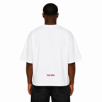 Back view of Black male model wearing the Trini Born oversized white T-shirt featuring subtle red Trini Born logo near the lower back on a clean white studio background.