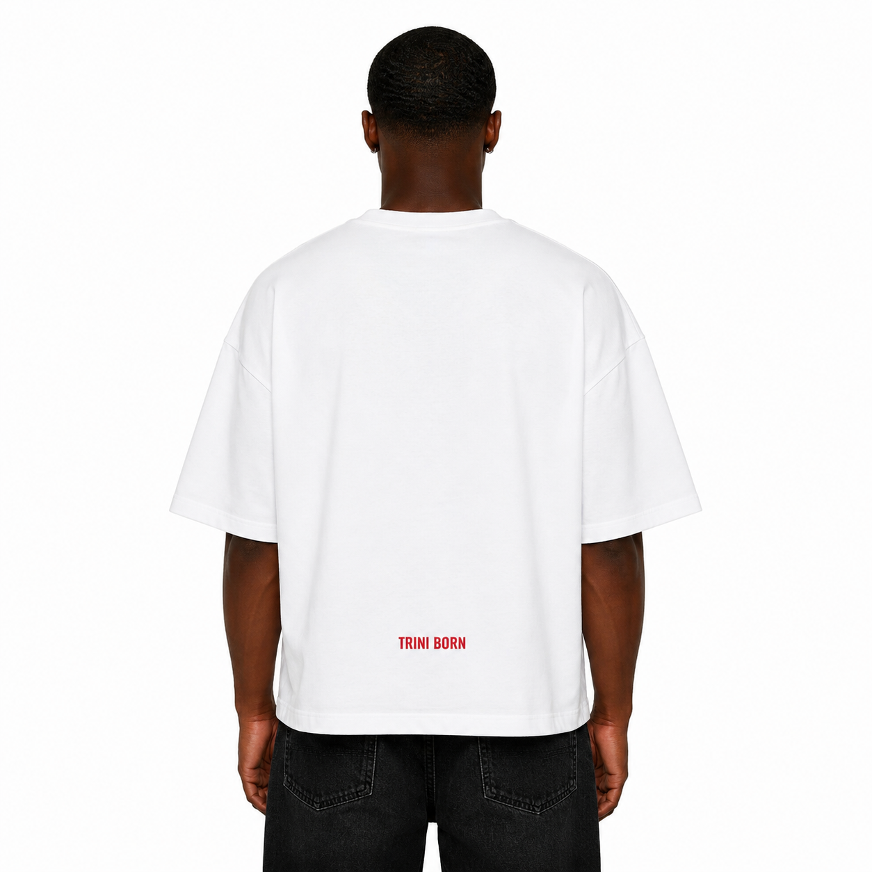 Back view of Black male model wearing the Trini Born oversized white T-shirt featuring subtle red Trini Born logo near the lower back on a clean white studio background.