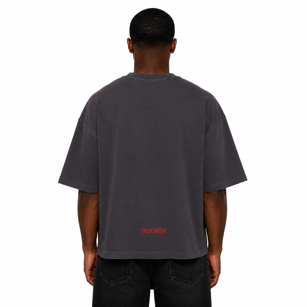 Back view of Black male model wearing the Trini Born oversized charcoal T-shirt with red Trini Born logo near the hem on a white studio background.