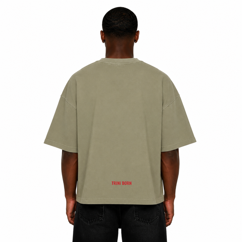 Back view of Black male model wearing the Trini Born oversized Gray Green T-shirt featuring a red Trini Born logo near the lower back on a white studio background.