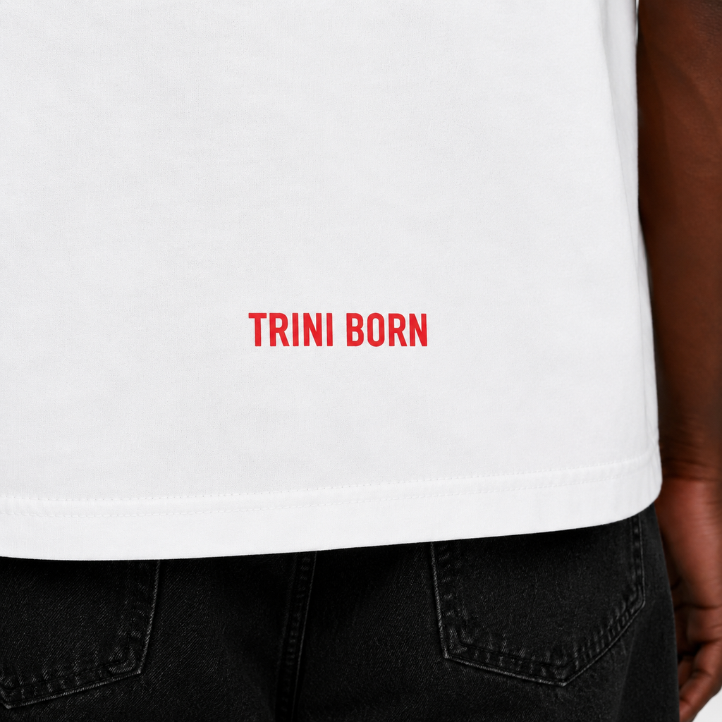 Close-up of the red Trini Born logo printed near the lower back hem of the oversized white T-shirt, highlighting premium cotton fabric and stitching details.
