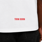 Close-up of the red Trini Born logo printed near the lower back hem of the oversized white T-shirt, highlighting premium cotton fabric and stitching details.