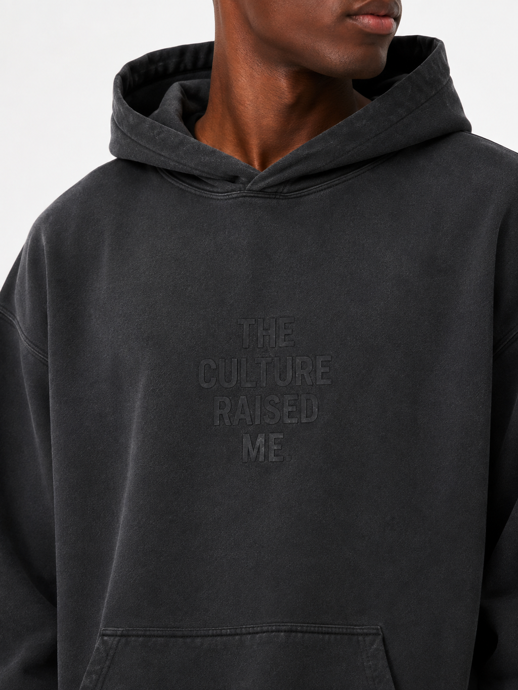 Close-up of the washed black Trini Born Culture Raised Me heavyweight oversized hoodie on a Black male model, showing the tonal THE CULTURE RAISED ME. chest design and sunfaded cotton finish.