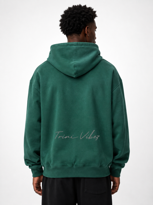 Back view of Black male model wearing the Trini Born Culture Raised Me heavyweight oversized hoodie in washed green with tonal Trini Vibez script.