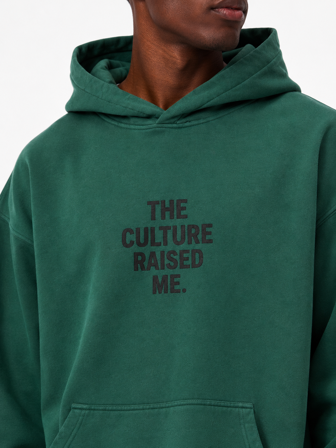 Close-up of the washed green Trini Born Culture Raised Me heavyweight oversized hoodie on a Black male model, showing the tonal THE CULTURE RAISED ME. chest design and cotton texture.