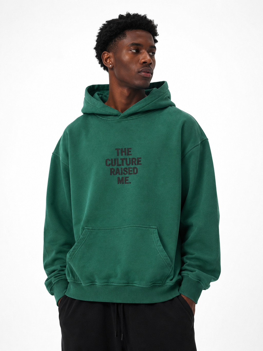 Black male model wearing the Trini Born Culture Raised Me heavyweight oversized hoodie in washed green, front view with tonal THE CULTURE RAISED ME. graphic.