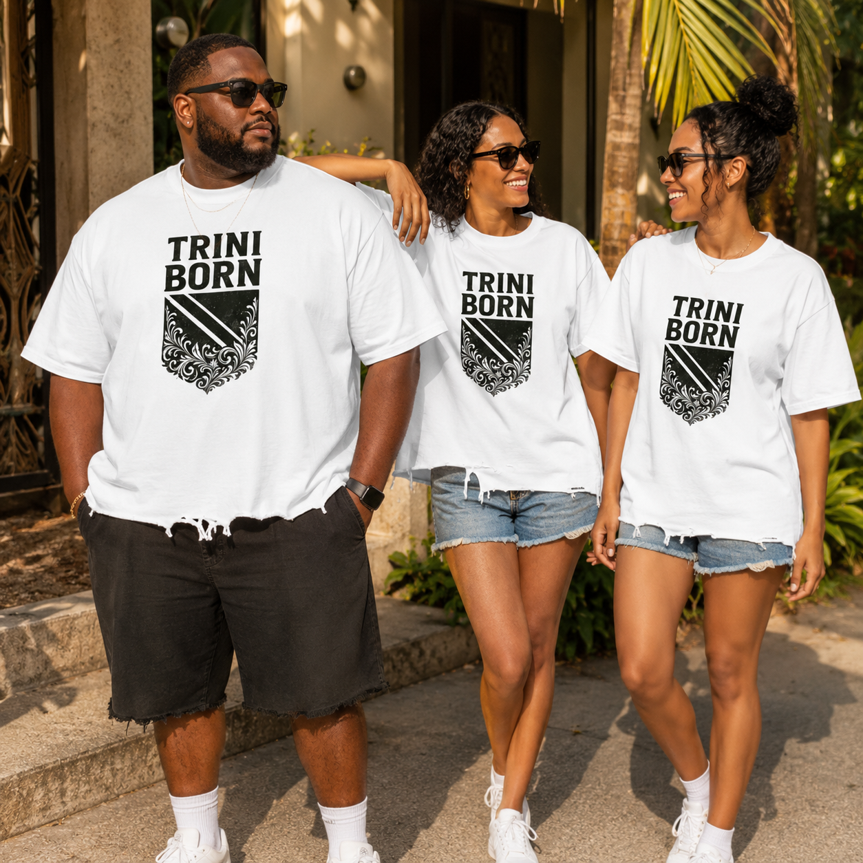 Three people wearing white Trini Born Culture Tee in outdoor lifestyle setting, oversized Trinidad streetwear showing crest graphic and raw hem.