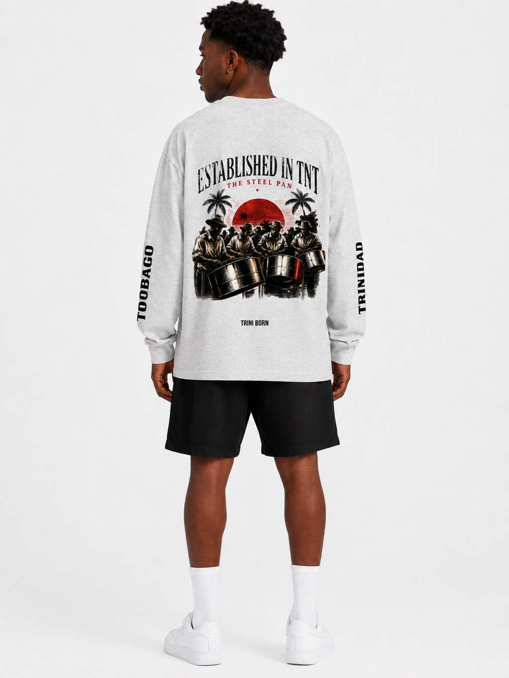 Back view of Black male model wearing the oat gray Trini Born Steelpan Heritage oversized long sleeve with steelpan musician artwork and Trinidad and Tobago sleeve text.