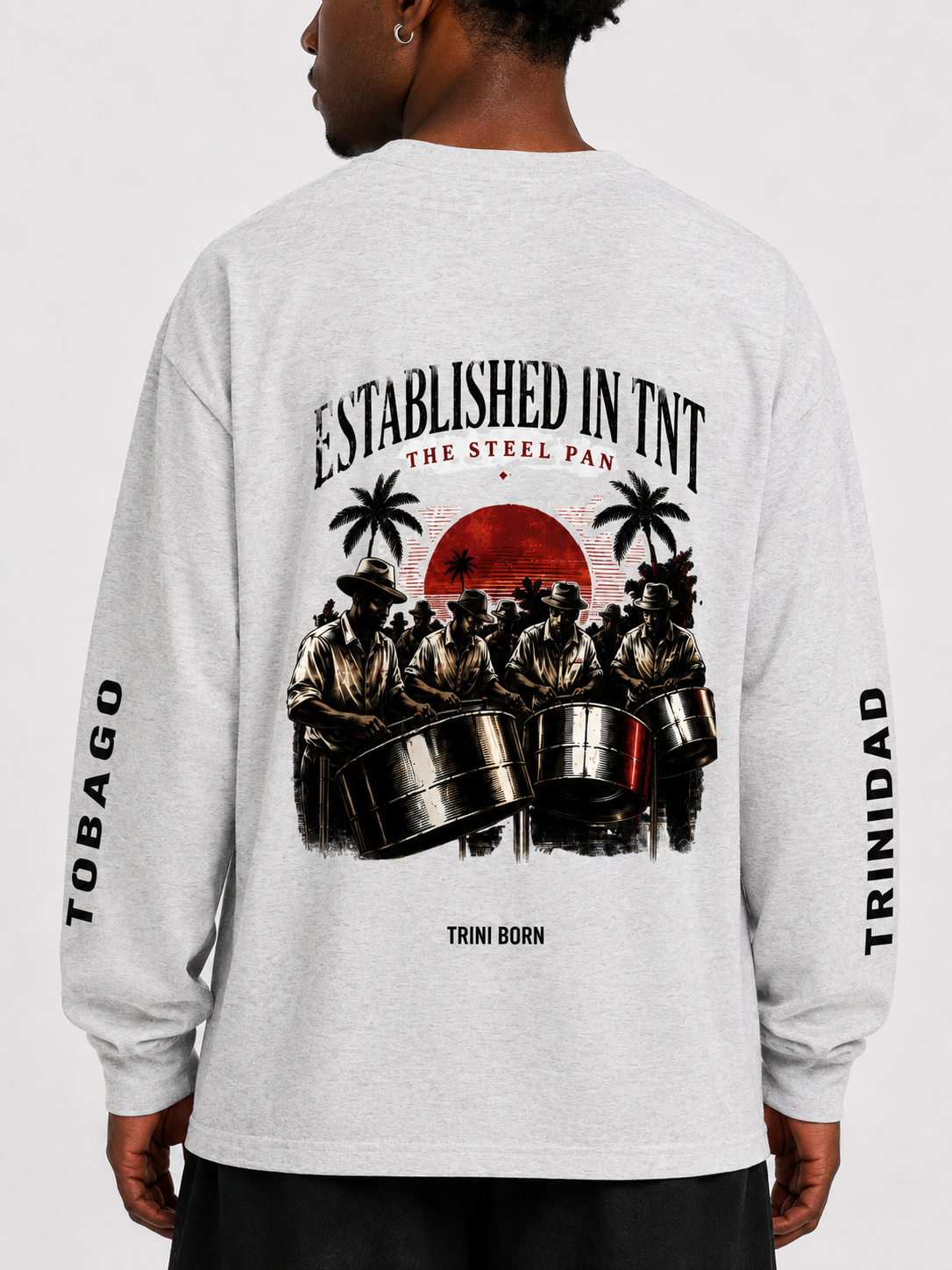 Close-up of the back of the white Trini Born Steelpan Heritage oversized long sleeve showing steelpan musicians, sunset artwork and Trini Born branding.