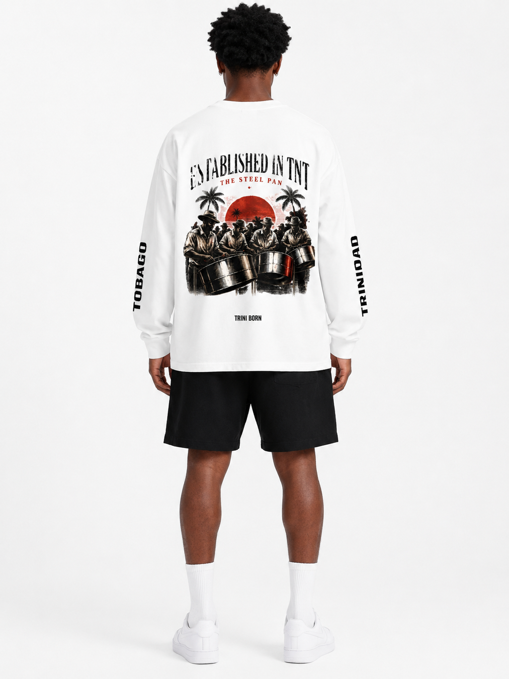 Black male model wearing the Trini Born Steelpan Heritage oversized long sleeve in white, front view with Established in TNT, TNT and The Steel Pan graphics.