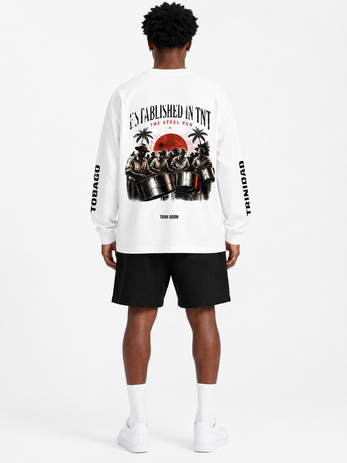 Black male model wearing the Trini Born Steelpan Heritage oversized long sleeve in white, front view with Established in TNT, TNT and The Steel Pan graphics.
